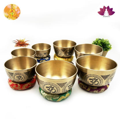 Set of brass cups with Om symbol on colorful coasters against a white background