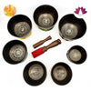 Set of black singing bowls with decorative symbols and wooden striking tools on a white background.