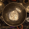 Decorative metal bowl with intricate designs and a central figure, surrounded by other similar items.