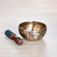 Full Moon Jhumkana singing bowl with wooden striker laid beside it, displaying engraved rim lines, fire-spot patina and carved symbol — made in Nepal