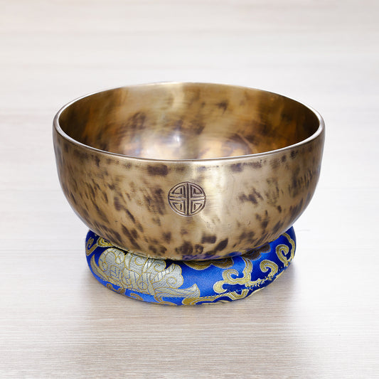 Handcrafted Full Moon Jhumkana singing bowl with fire-spot patina and laser-carved symbol, resting on a blue brocade cushion — made in Nepal