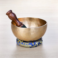 Full Moon Jhumkana singing bowl engraved with Om Mani Padme Hum Tibetan mantra, with wooden mallet resting inside on blue brocade cushion — made in Nepal