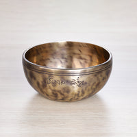 Full Moon Jhumkana singing bowl with wooden mallet and blue brocade cushion, showing fire-spot patina and laser-carved symbol — handcrafted in Nepal