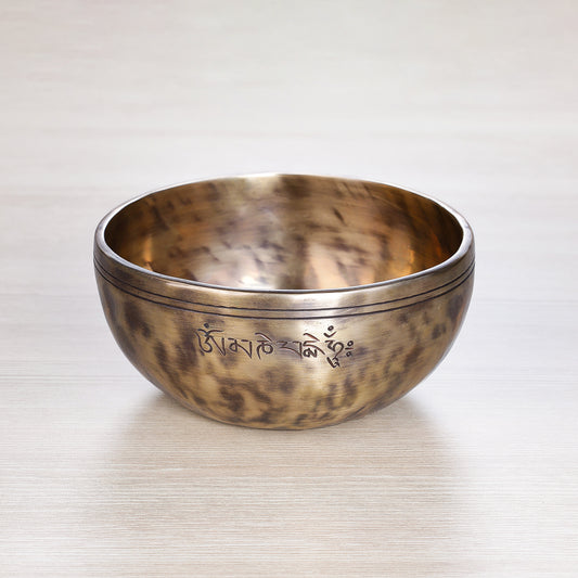 Full Moon Jhumkana singing bowl with wooden mallet and blue brocade cushion, showing fire-spot patina and laser-carved symbol — handcrafted in Nepal