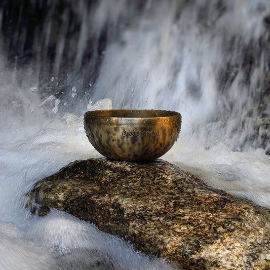 Tibetan singing bowl on a rock with a waterfall in the background
