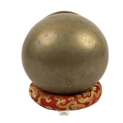 Bronze ball on a decorative red and gold stand against a beige background