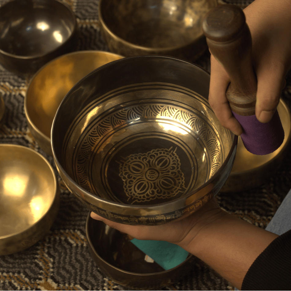 Person holding a brass singing bowl with intricate designs on a textured surface