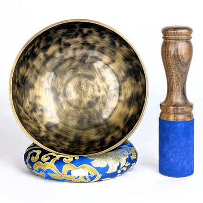 Tibetan singing bowl with decorative base and wooden striker on a white background